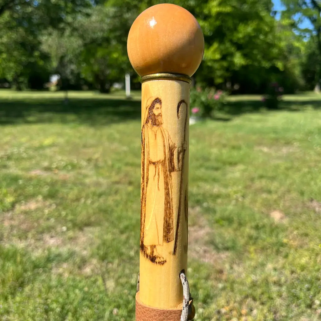 Full upper shaft showing Jesus shepherd wood-burned carving with ball handle, outdoor setting
