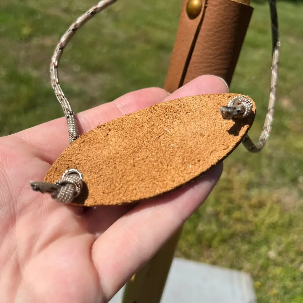 Hand holding suede/leather wrist strap (back side), paracord attachment visible