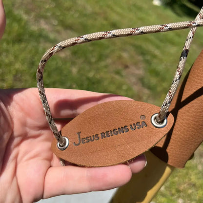 Jesus Reigns USA branded leather oval tag with paracord, resting on cane