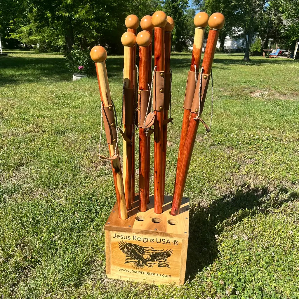 Handmade hardwood display box says Jesus Reigns USA on it.  It is holding 12 red cedar ball Knob walking canes with different color variations of red cedar.