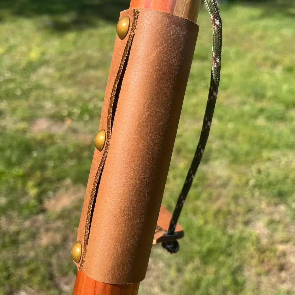 Leather grip with brass buttons on red cedar ball knob walking cane, camo paracord wrist strap detail
