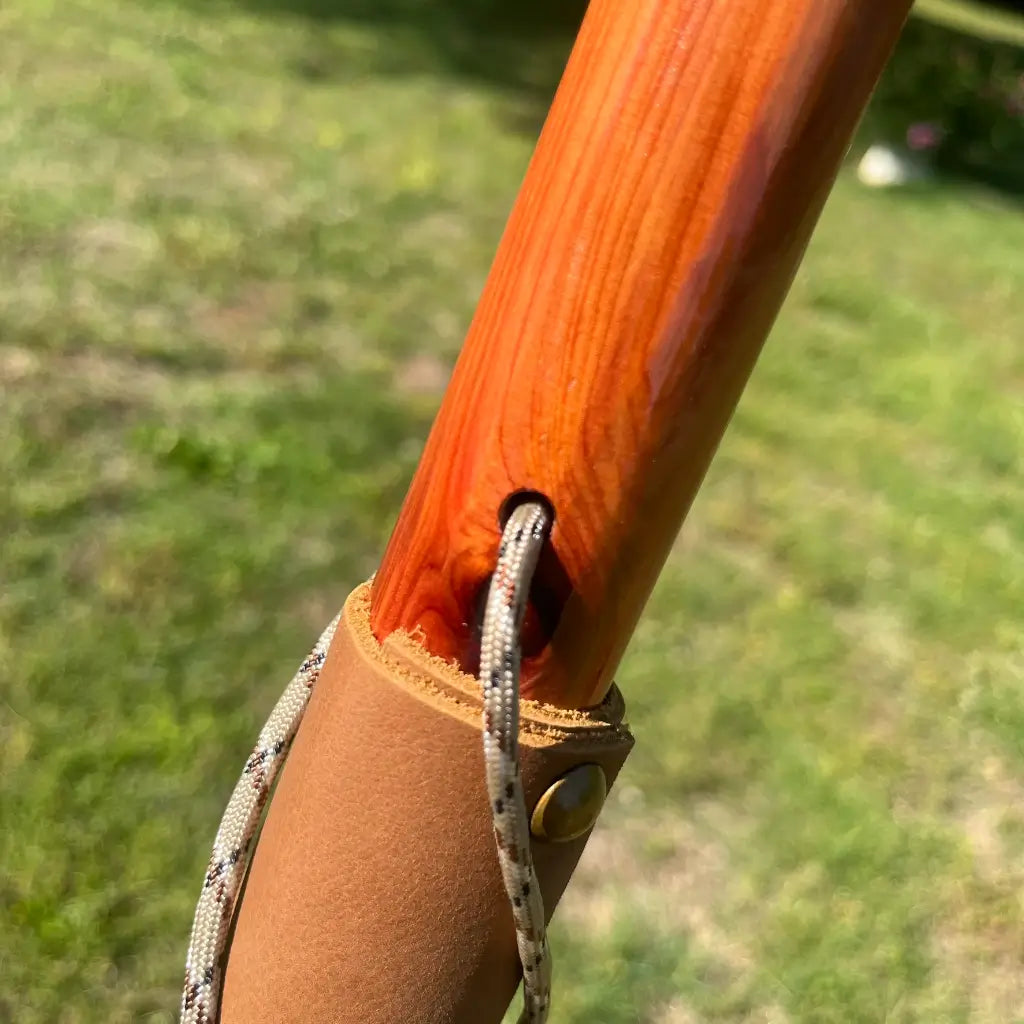 Top edge of leather grip meeting red cedar shaft with brass grommet and paracord wrist loop detail

