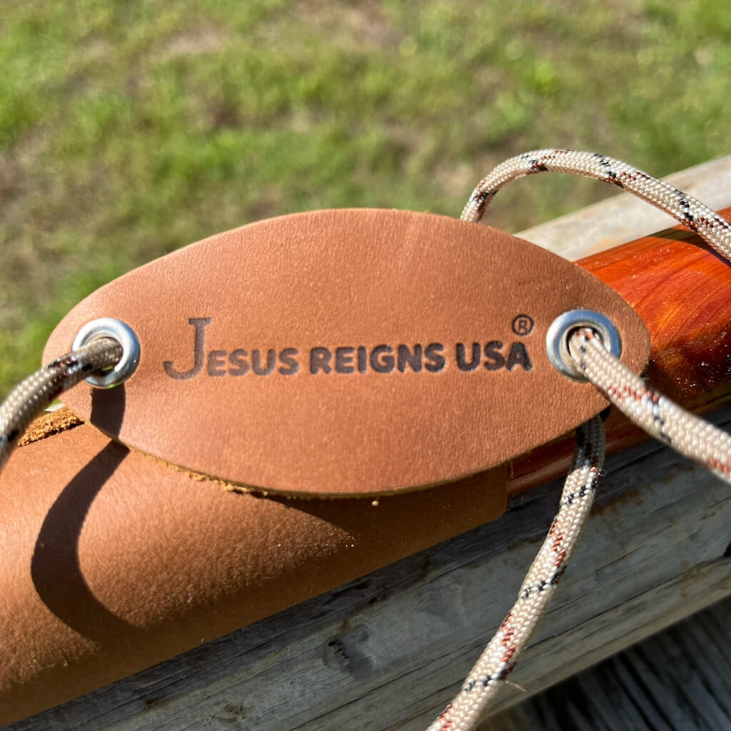 Jesus Reigns USA® leather brand tag with brass grommets and paracord wrist strap on red cedar walking cane
